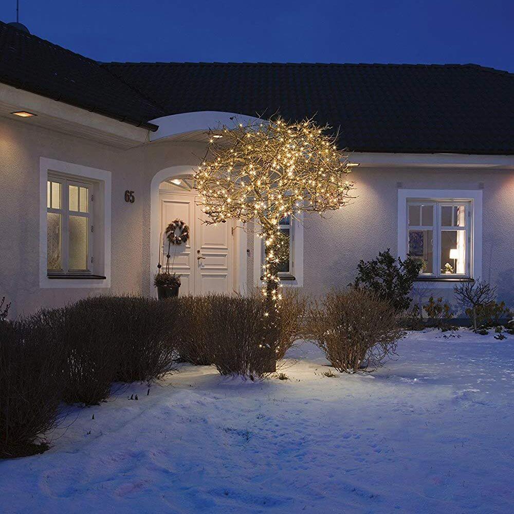 16m Micro LED Lichterkette mit Aufroller 40 bernsteinfarbene Dioden IP44 beleuchtet einen Baum im Schnee vor einem Haus.