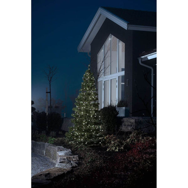 Extensão de 89m de corrente de luz LED Micro com 100 Diodos Brancos Frios IP44 ilumina uma árvore de Natal à noite.