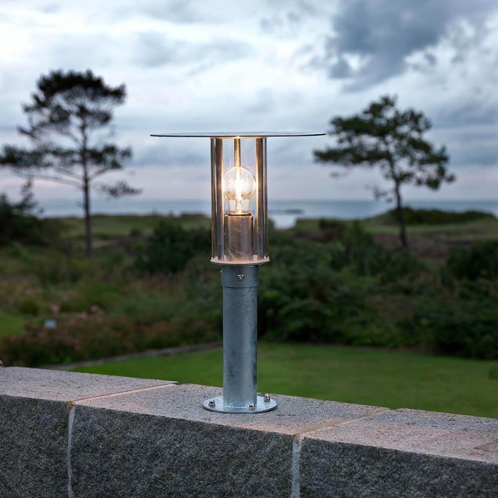 Mode Sockelleuchte galvanisierter Stahl, klares Polycarbonat Glas auf einer Gartenmauer mit Blick auf die Landschaft.