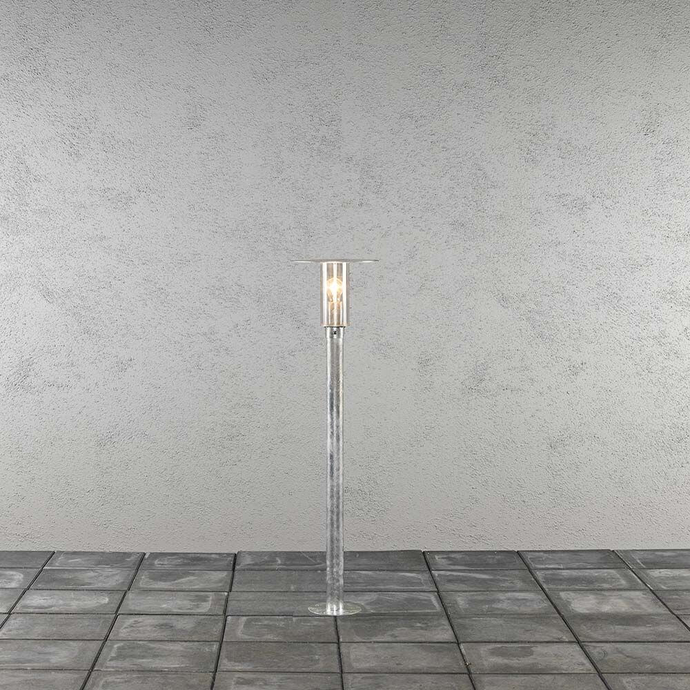Mode Wegeleuchte 111cm galvanisierter Stahl, klares Polycarbonat Glas auf einem grauen Pflastersteineboden.