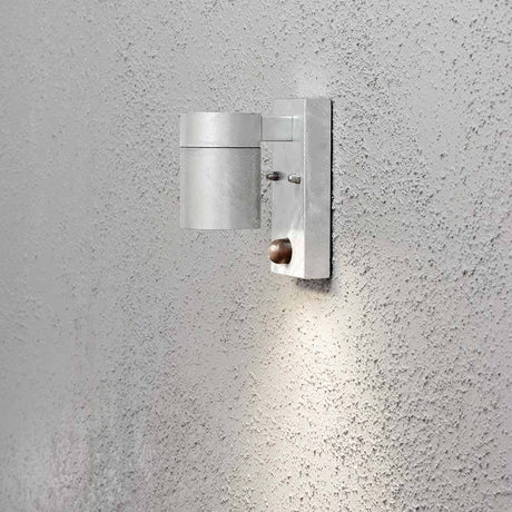 Modena Luminária de parede exterior com sensor de movimento em aço montada numa parede áspera.