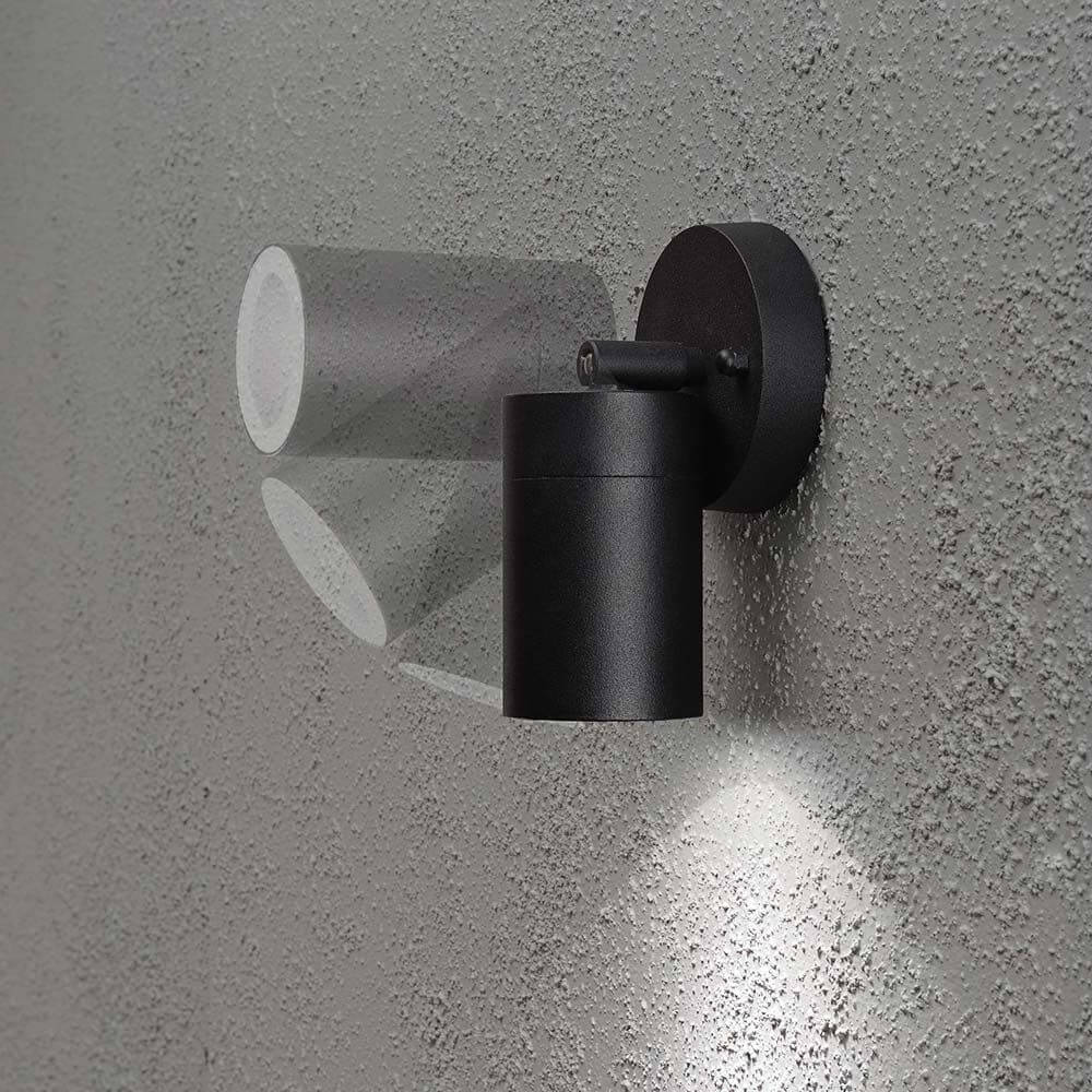 Modena Energiespar Wandspot schwenkbar Schwarz, klares Glas an einer Wand montiert, mit Lichtschein.