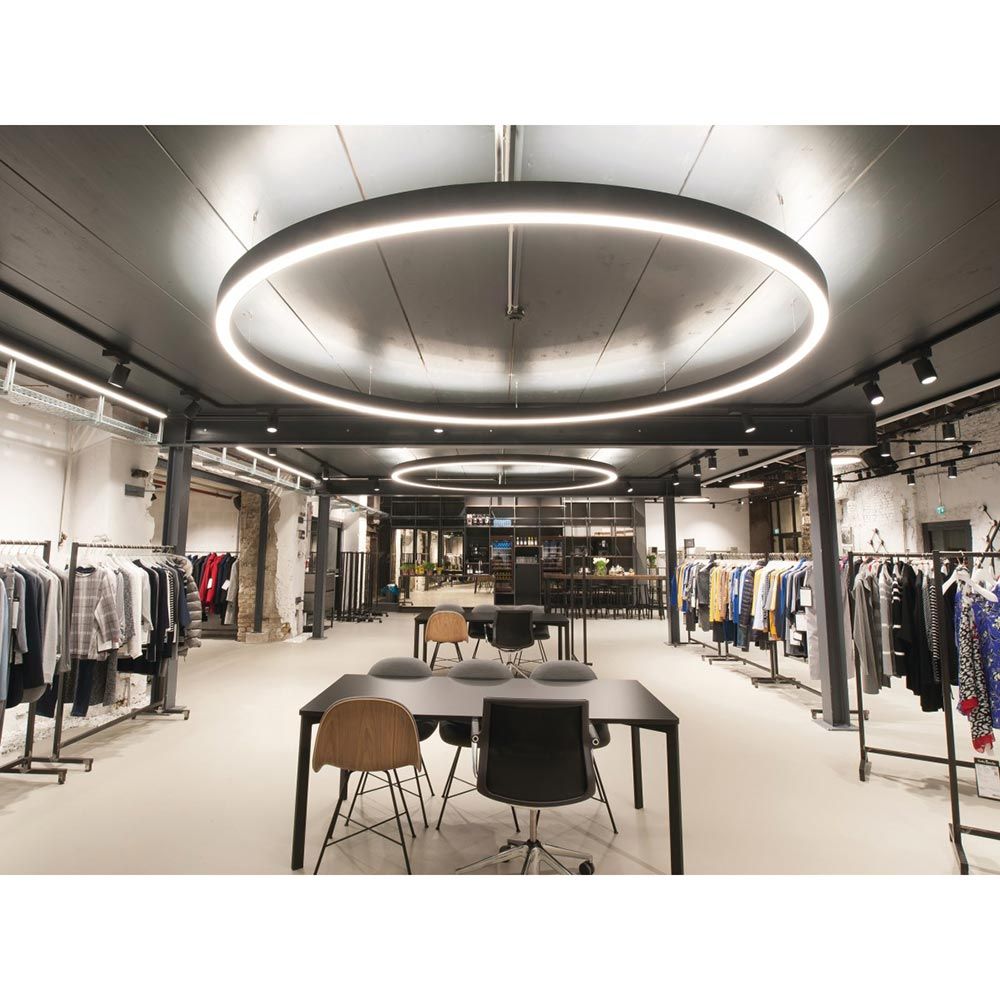Moderne Rinq LED Ring-Hängelampe in schwarzem Aluminium in einem stilvollen Verkaufsraum mit Stuhl und Tisch.