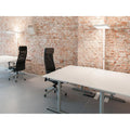 Moderne Büroumgebung mit System Büro Stehlampe und ergonomischen Stühlen vor einer Backsteinwand.