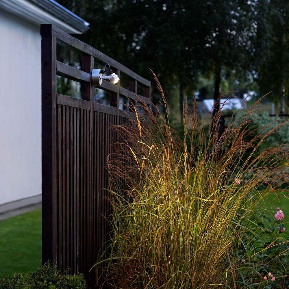 Monza LED Außen-Wandleuchte schwenkbar massives Aluminium an einem Holzzaun in einem Garten.