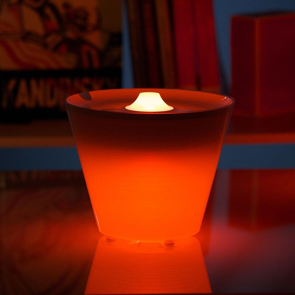 Rotaliana Multipot+ Tischleuchte Kabelcontainer + Ladestation Chrom in leuchtendem Orange auf Tisch.