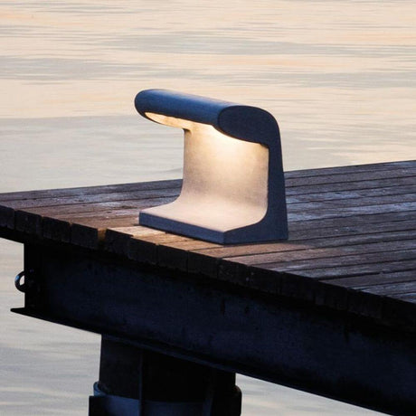 Nemo Borne Béton Petite Outdoor LED Tischlampe IP44 auf einem Holztisch am Wasser bei Sonnenuntergang.
