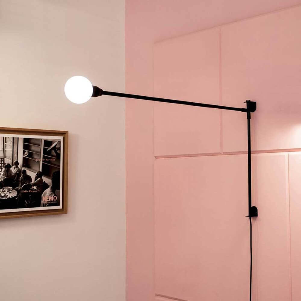 Nemo Potence Pivotante Mini Wandlampe 100cm an einer Wand mit pinkem Hintergrund.
