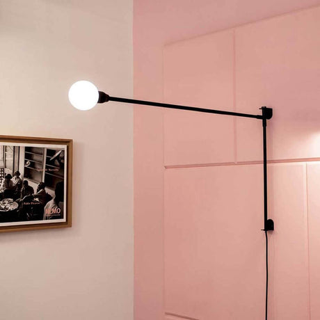 Nemo Potence Pivotante Mini Wandlampe 100cm an einer Wand mit pinkem Hintergrund.