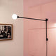 Nemo Potence Pivotante Mini Wandlampe 100cm an einer Wand mit pinkem Hintergrund.