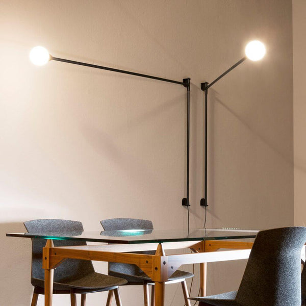 Nemo Potence Pivotante Wandlampe 200cm an einer Wand über einem Tisch mit modernen Stühlen.