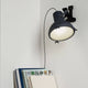 Nemo Projecteur 165 Klemmleuchte an einer Wand montiert, beleuchtet eine Bücherablage mit diffusem Licht.