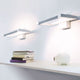 Nemo Spigolo LED Wandleuchte 360° drehbar an einer Wand über einer Ablage mit Büchern und einem Sparschwein.