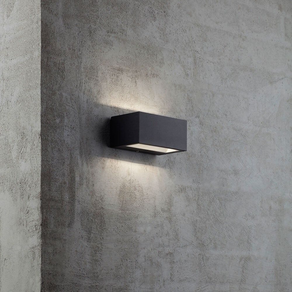 Nene LED Außen-Wandleuchte IP54 Schwarz an einer Wand aus Beton, strahlt sanftes Licht nach oben und unten.