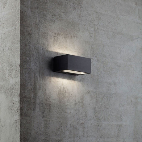 Applique da esterno LED Nene IP54 nera su una parete in cemento, diffonde una luce soffusa verso l'alto e verso il basso.