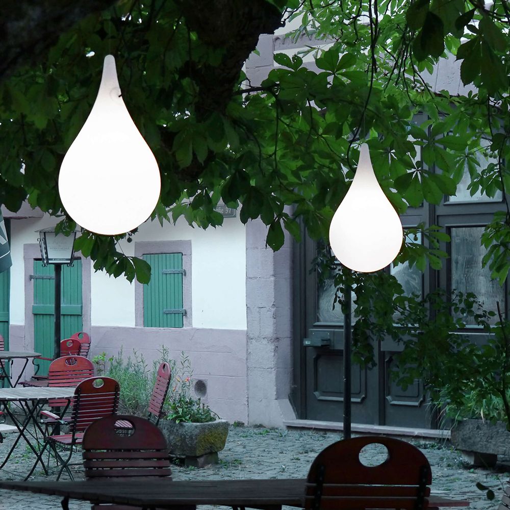 Tropfenförmige Pendelleuchte aus Kunststoff, aufgehängt mit Stahlseil, in einer Gartenumgebung.