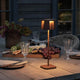 Nice LED Outdoor USB-Tischlampe CCT auf einem Tisch, beleuchtet und umgeben von Essen und Getränken.