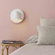 Noon Wandlampe Weiß an einer rosa Wand, ideal als modernes Lese- und Stützlicht im Schlafzimmer.