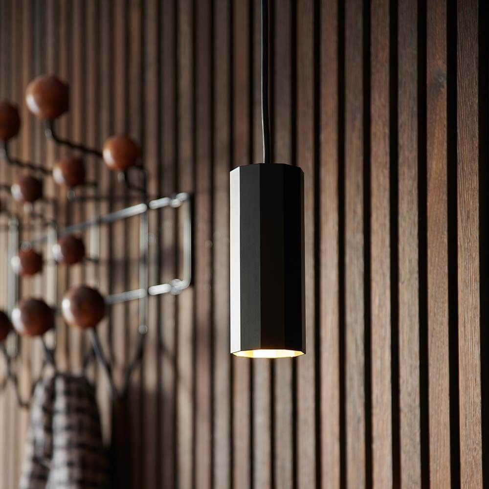 Alanis Pendelleuchte: stilvolle, minimalistische Pendelleuchte mit 10-seitigem Profil, hängend an einer Holzwand.