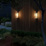 Coupar Außenwandleuchte mit sanftem Licht, modernes Design an einer Holzfassade im Garten.