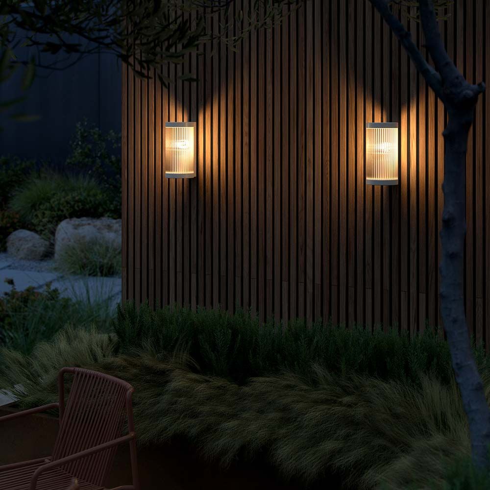 Coupar Außenwandleuchte von Says Who mit sanftem Licht auf einer Holzverkleidung im modernen Garten.