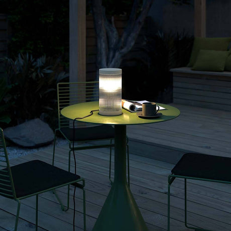 Coupar Tischleuchte auf einem grünen Tisch im Freien, ideal für abendliche Entspannung.
