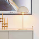 Ellen Tischleuchte Beige auf einem Sideboard mit modernem Kunstwerk im Hintergrund, sorgt für sanftes Licht.