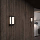 LED-sensorvegglampe Nestor IP44 dimbar svart montert på en trevegg.