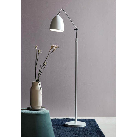 Moderne Stehleuchte Alexander Weiß neben einer Vase mit Blumen auf einem Teppich.