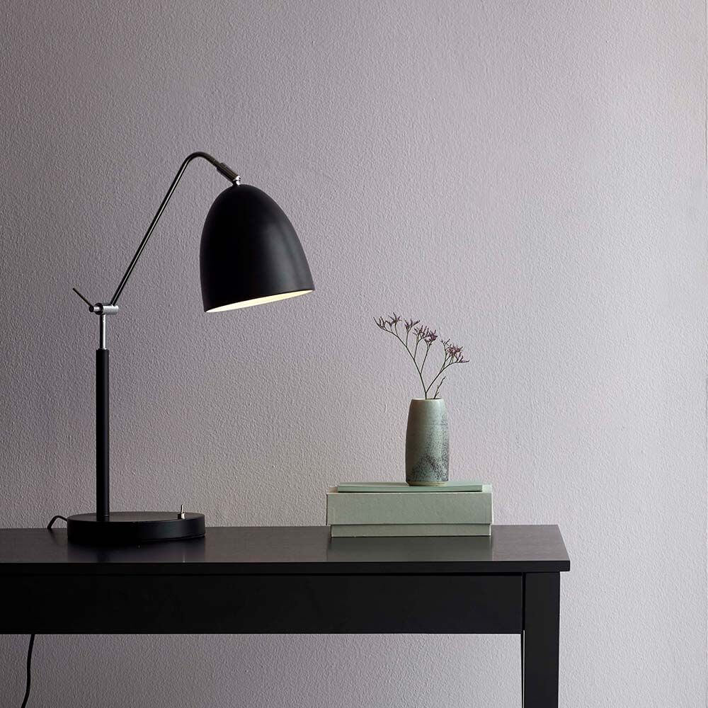 Tischlampe Alexander Schwarz auf einem schwarzen Tisch neben einer Vase mit Blumen und Büchern.