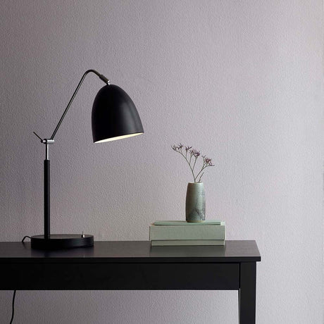 Lampe de table Alexander noire sur une table noire à côté d’un vase avec des fleurs et des livres.