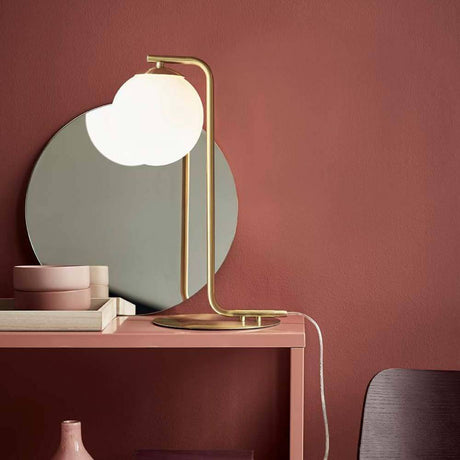 Lampe de table Grant laiton, opale blanche sur une table devant un mur aux tons chauds.
