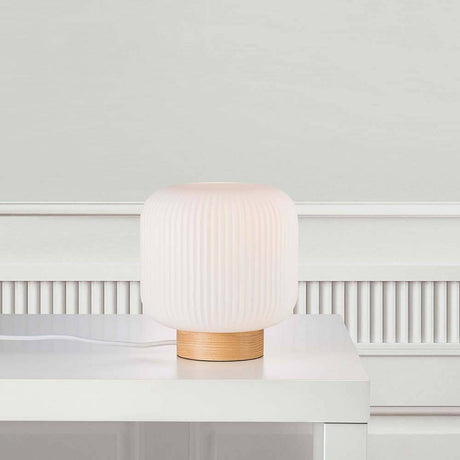 Tischleuchte Milford Braun, Opalweiß auf einem Tisch mit warmem Licht und Holzsockel.