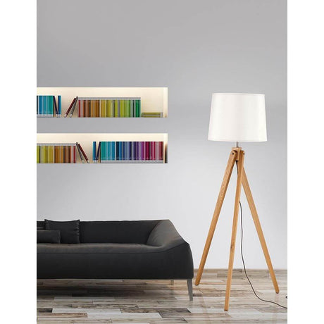 Alma tre-benet gulvlampe i naturtre, hvit ved siden av en moderne sofa og fargerike bokhyller.