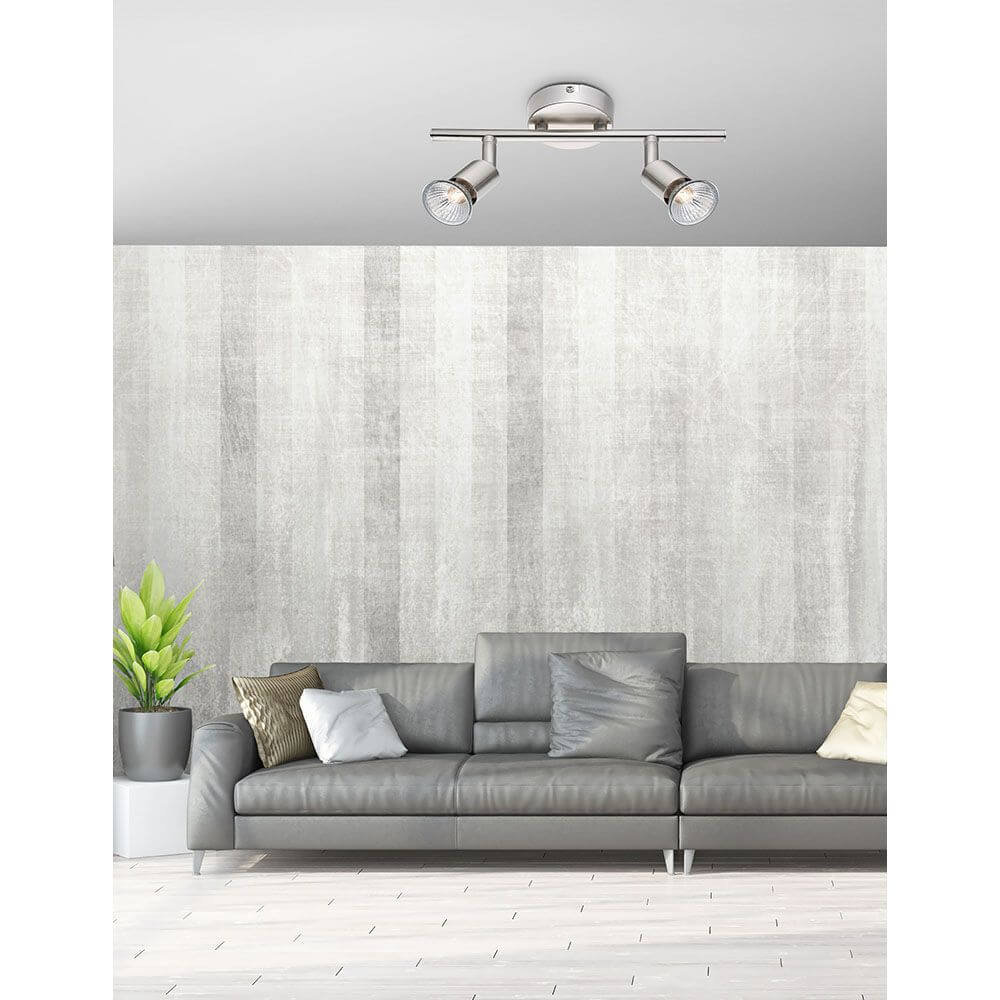 Base Balkenstrahler 2-flammig mit drehbaren Strahlern in modernem Design über einem grauen Sofa.