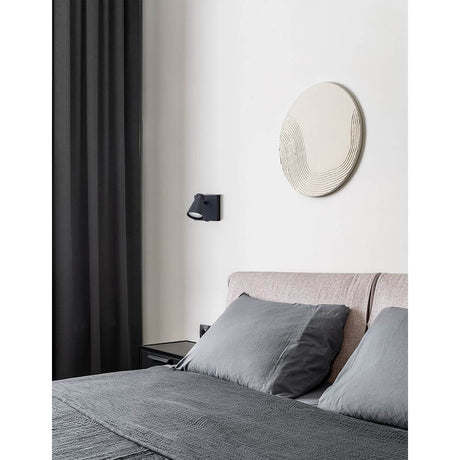 Dublin LED spot mural sur un mur au design moderne au-dessus d'un lit avec des coussins gris.