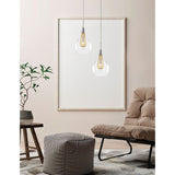 Moderne Filo Glas-Hängelampe in klar und gold in stilvollem Wohnzimmer mit Pflanze und gemütlichem Stuhl.