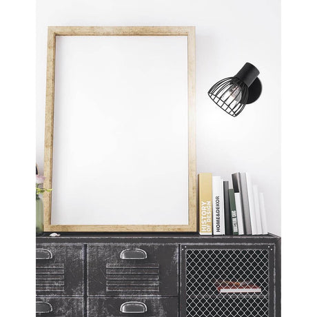 Fiumicino wall spotlight matte black on a wall above a modern sideboard with picture frames and books.