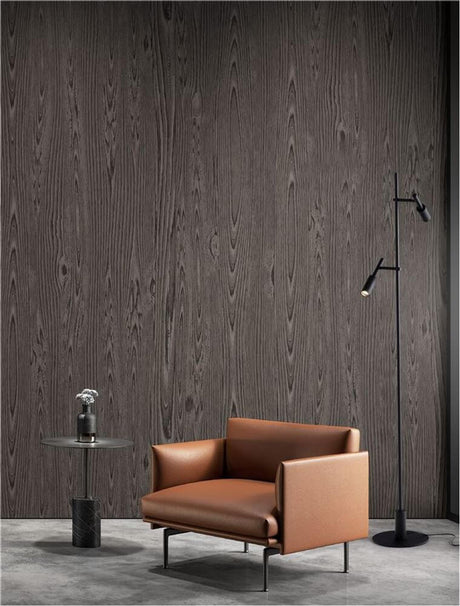 Lampadaire Joy LED noir 161 cm à côté d’un fauteuil et d’une table modernes devant un mur aspect bois.