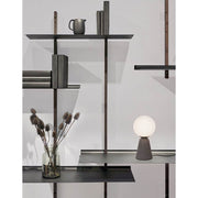 Lampe de table Orion en béton sur une étagère moderne avec des livres et un vase.
