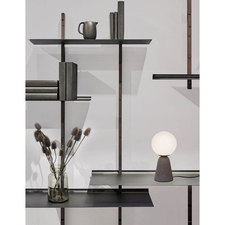 Orion table lamp in concrete on a modern shelf with books and a vase.