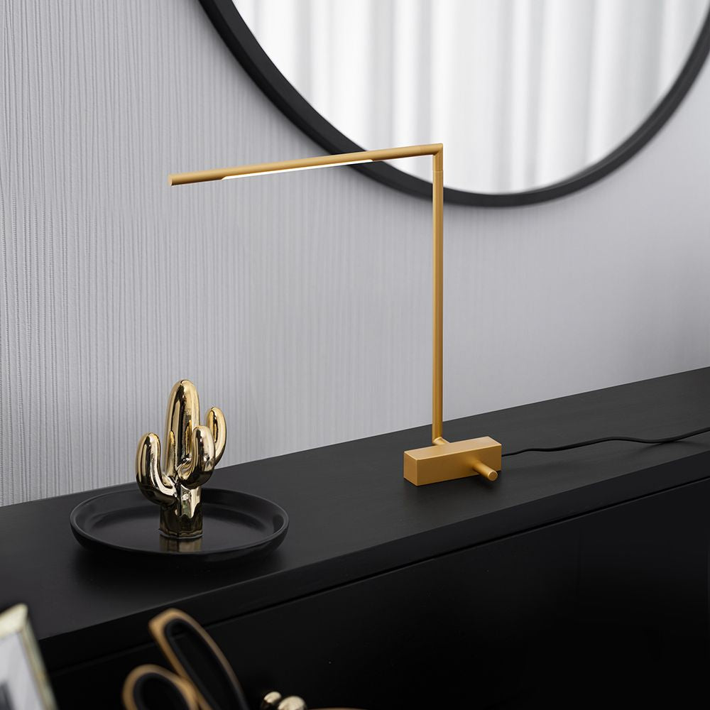 Moderne Raccio LED Tischleuchte in Gold auf schwarzem Tisch mit Kaktus-Dekor und Spiegel im Hintergrund.
