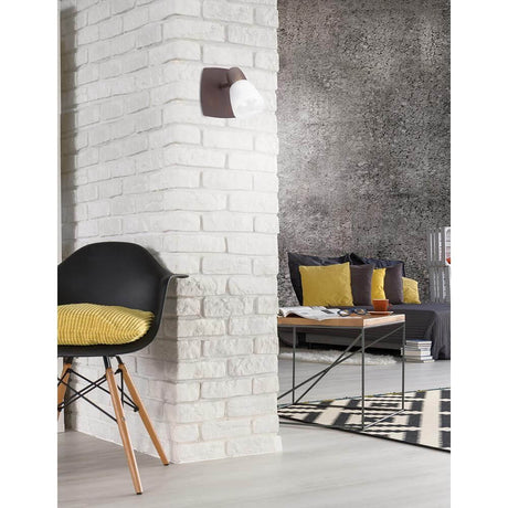 Reggio wall spotlight in rust color on a white brick wall in a modern living space with decorative furnishings.