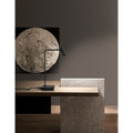 Sicily LED Tischlampe aus schwarzem Metall auf einem modernen Holztisch mit Kunstwerk im Hintergrund.