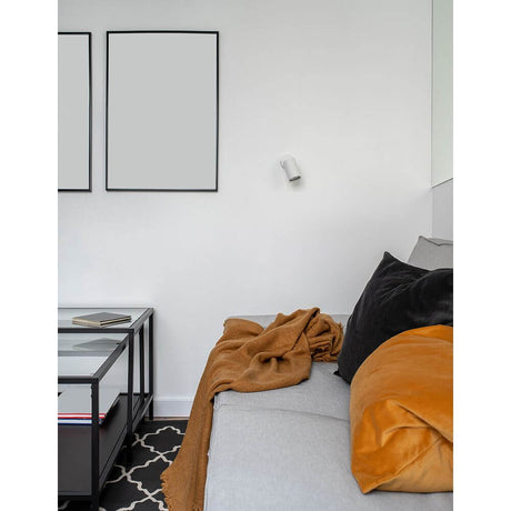 Moderne Wan væglampe i metal på en væg over en sofa med puder og tæppe.