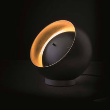 Oluce LED Tischleuchte Eva Schwarz, Goldfarben auf einem Tisch mit elegantem Design und einzigartiger Lichtwirkung.