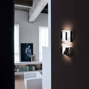 Oluce LED Wandlampe Kelly Chrom an einer Wand in einem modernen Wohnraum.
