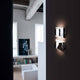 Oluce LED Wandlampe Kelly Chrom an einer Wand in einem modernen Wohnraum.