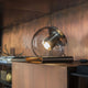 Oluce Tischlampe The Globe Antik Goldfarben auf einem Holztisch mit glänzender Oberfläche.