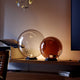 S.luce Orb Glaskugel Tischlampe in zwei Größen auf einem Regal, minimalistische Eleganz und moderne Beleuchtung.